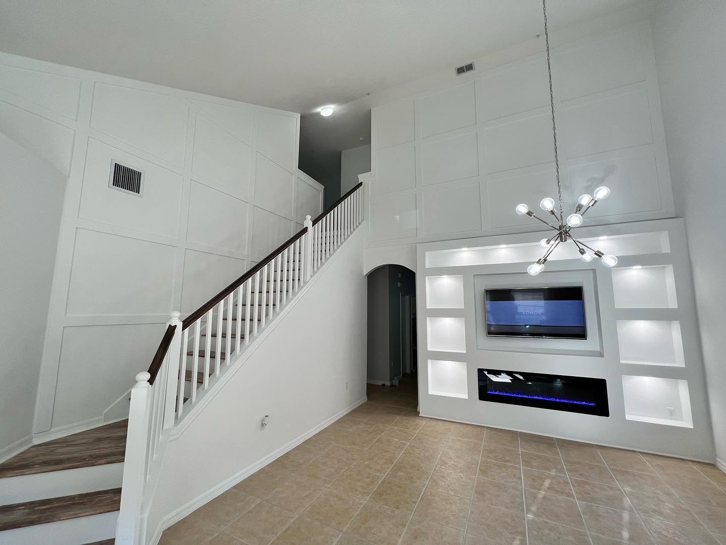 Double-height great room with grid-paneled walls, staircase and a custom lit-niche media wall.