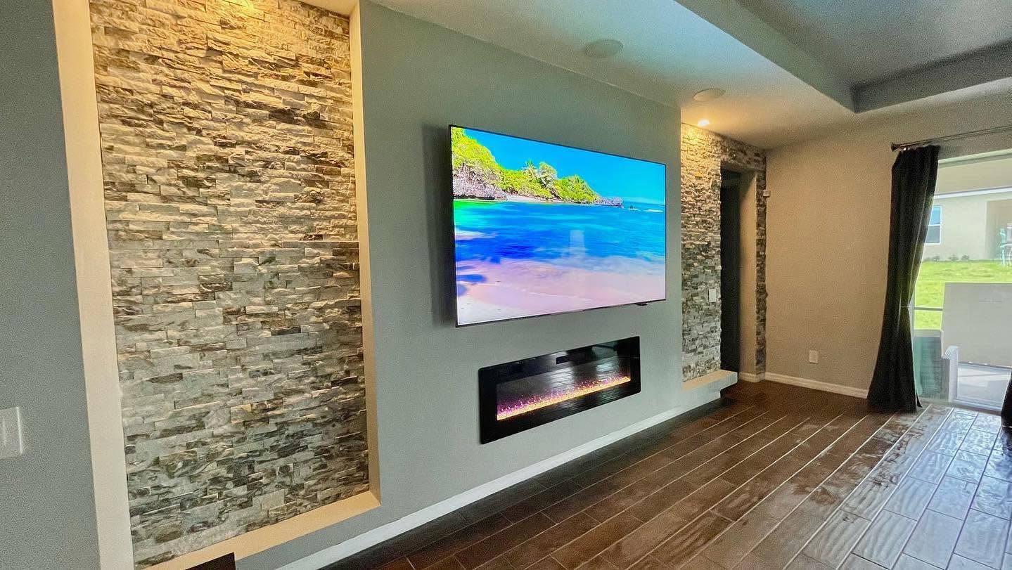 Living area with stacked-stone accent walls flanking a wall-mounted television and linear fireplace.