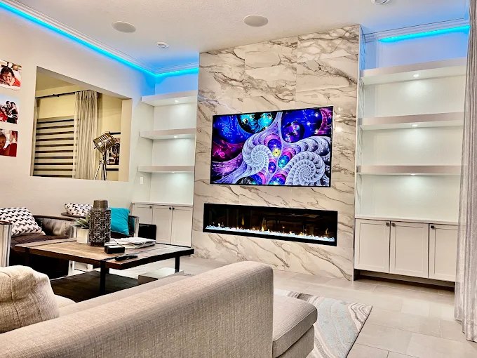 Living room marble feature wall with a linear fireplace, glass display shelving and blue cove lighting.