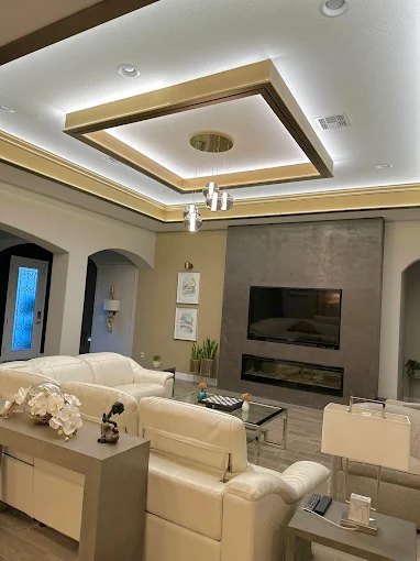 Living room with a layered coffered ceiling detail, wall-mounted television and linear fireplace.