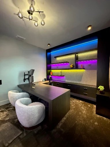 Lounge and bar area with a dark feature wall, seating and colour-changing LED lighting.