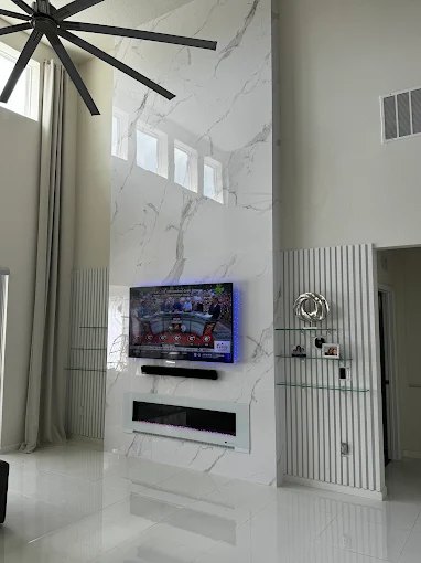Tall marble fireplace surround with a wall-mounted television, flanked by white fluted wall panels.