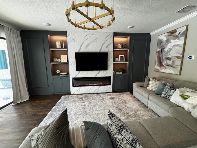 Marble-look media wall flanked by navy built-in cabinetry and lit display shelving, with a linear fireplace below the television.
