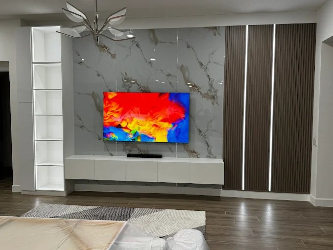 Marble-look media wall with a recessed television, flanked by dark vertical fluted panels and white built-in shelving.