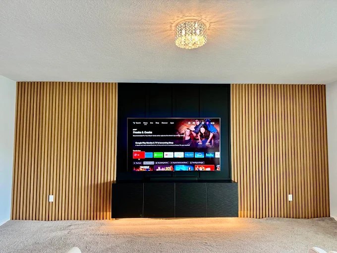 Full-width wood slat wall with a recessed television and dark built-in cabinet beneath.